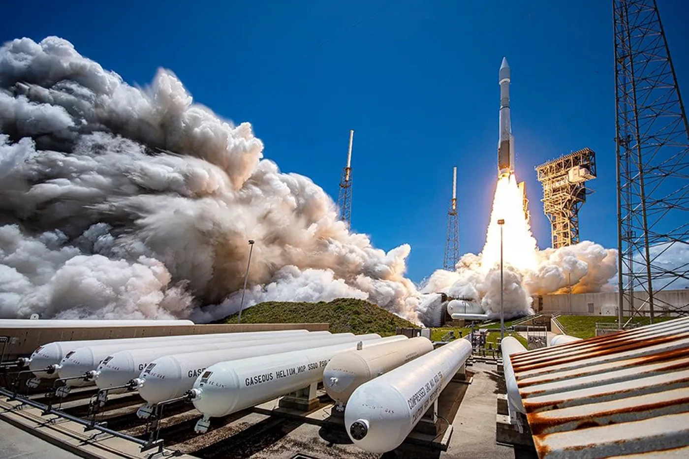 An Atlas V lifting off from the pad, with the exhaust plume rolling out across the launch complex.