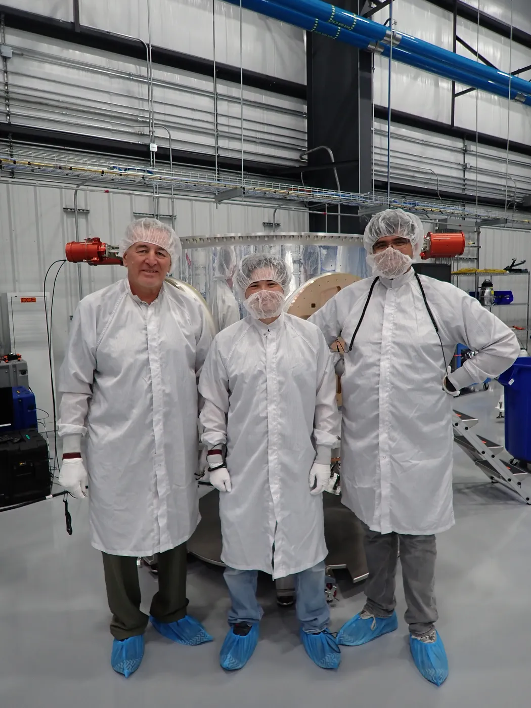 Three ALS staff in cleanroom garments standing in front of an assembled payload adapter structure.