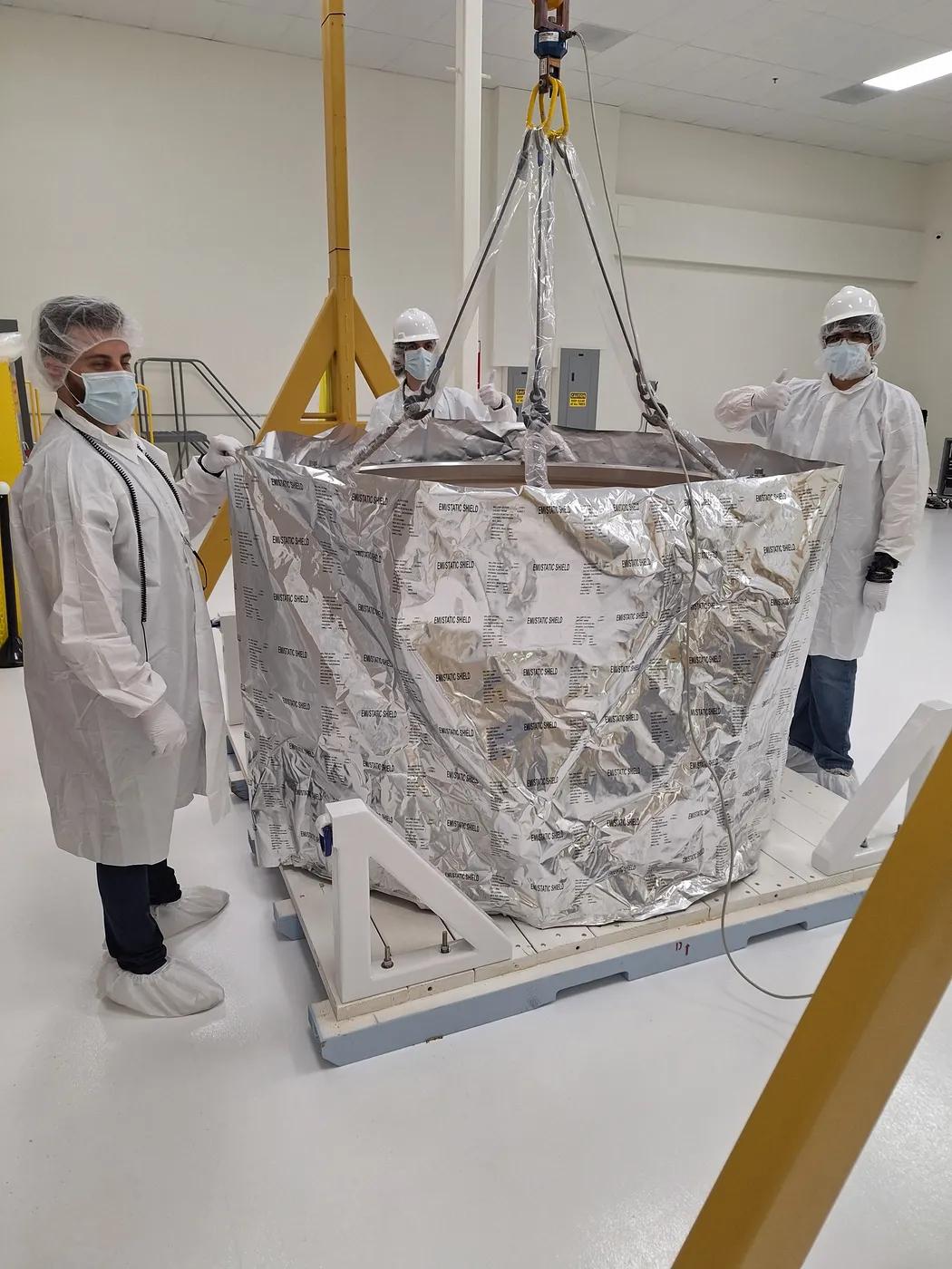 An integrated payload stack under an EMI-static shield being lifted by overhead crane onto its transport pallet.