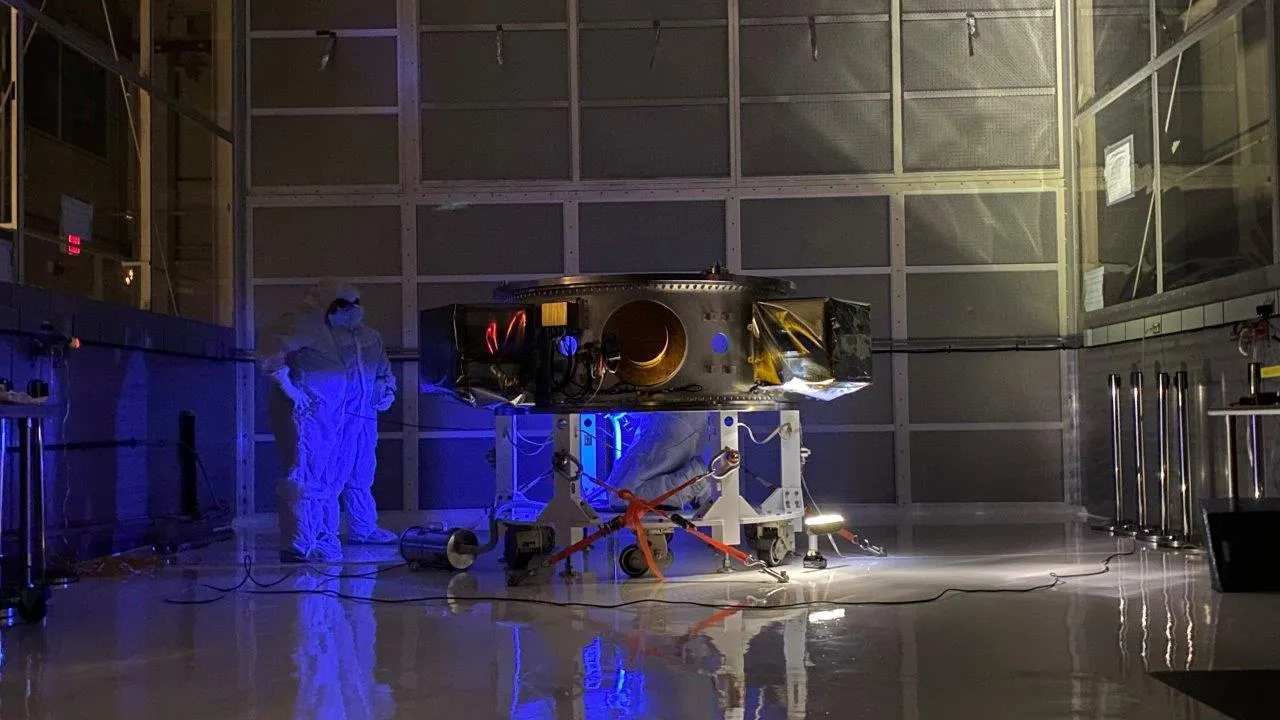 A contamination inspection under ultraviolet light, a technician surveying the payload adapter in a darkened high bay.