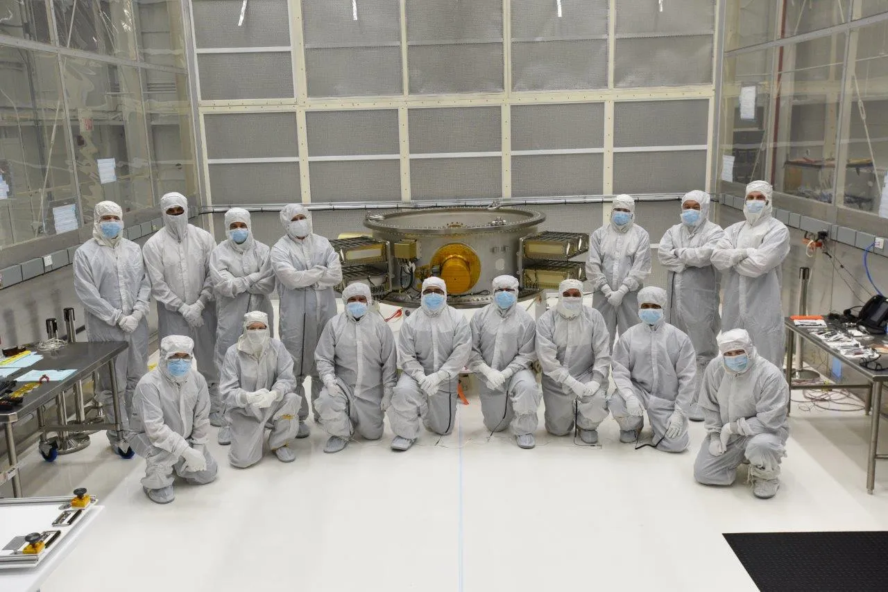 The full integration team assembled in the cleanroom around a completed payload stack before transport.