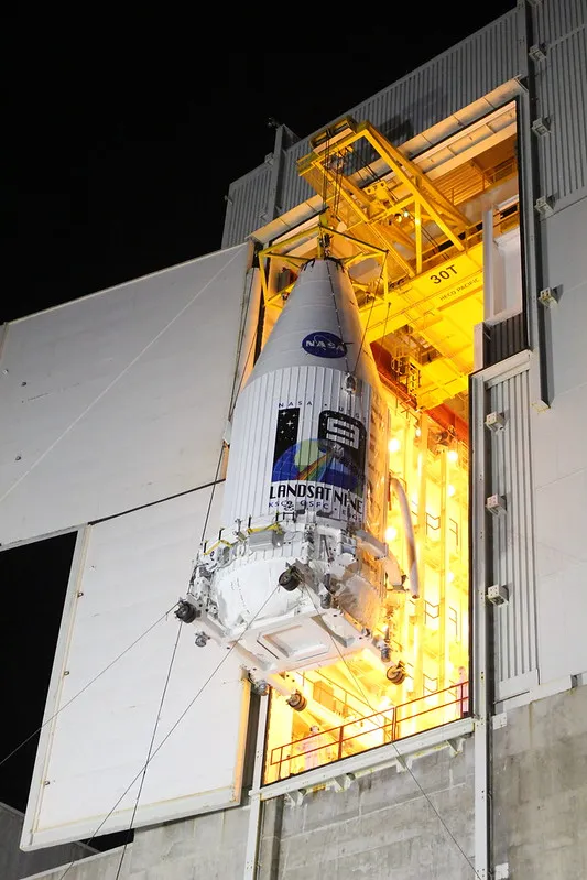 The encapsulated Landsat 9 payload being lifted into the launch vehicle integration tower at night.